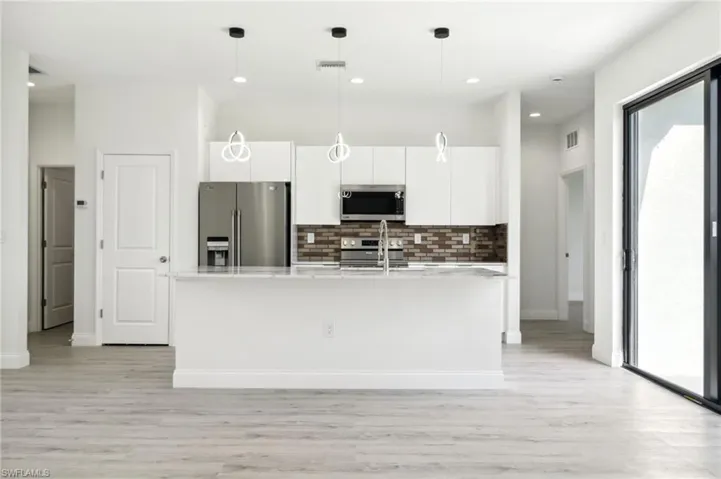 Kitchen featuring light wood-style flooring, light countertops, decorative backsplash, white cabinets, and appliances with stainless steel finishes