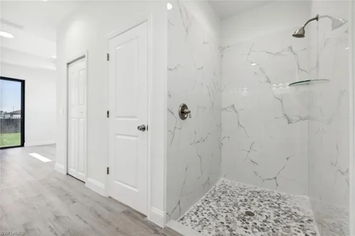 Bathroom featuring a marble finish shower, baseboards, and wood finished floors