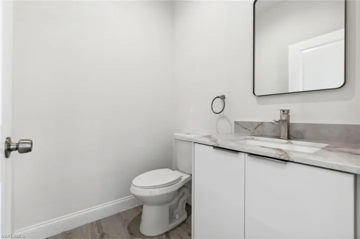 Half bath with vanity, toilet, baseboards, and wood finished floors