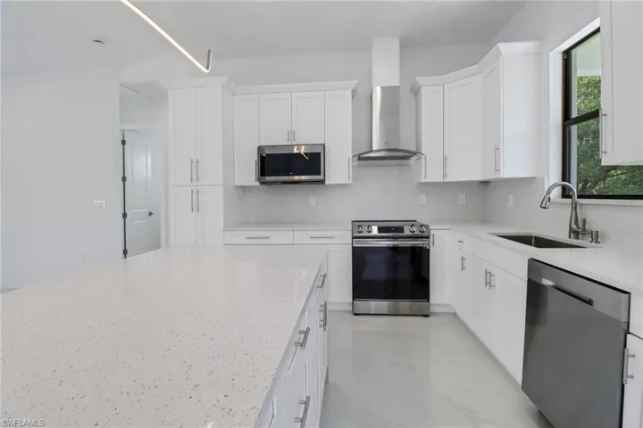 Kitchen with white cabinets, a sink, wall chimney range hood, appliances with stainless steel finishes, and decorative backsplash