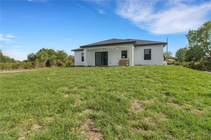 Back of property with a yard, stucco siding, and ceiling fan