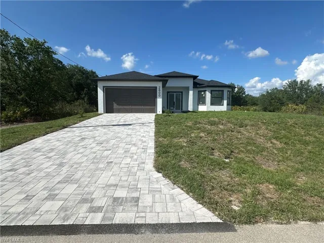 Prairie-style house featuring a front yard, decorative driveway, a garage, and stucco siding