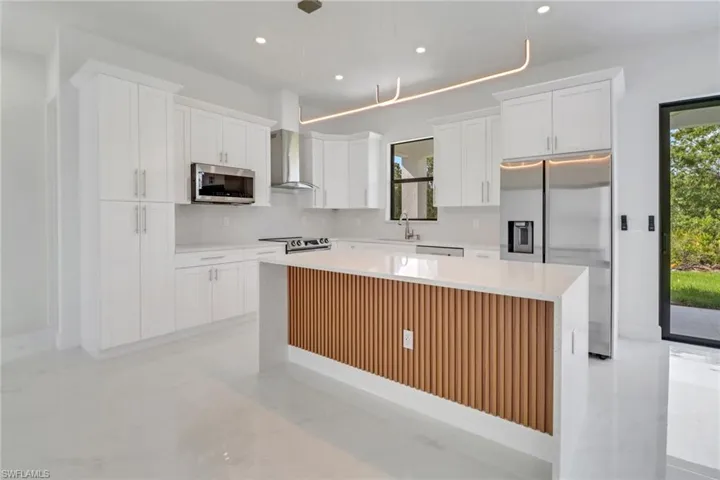 Kitchen featuring appliances with stainless steel finishes, wall chimney exhaust hood, white cabinets, and a kitchen island