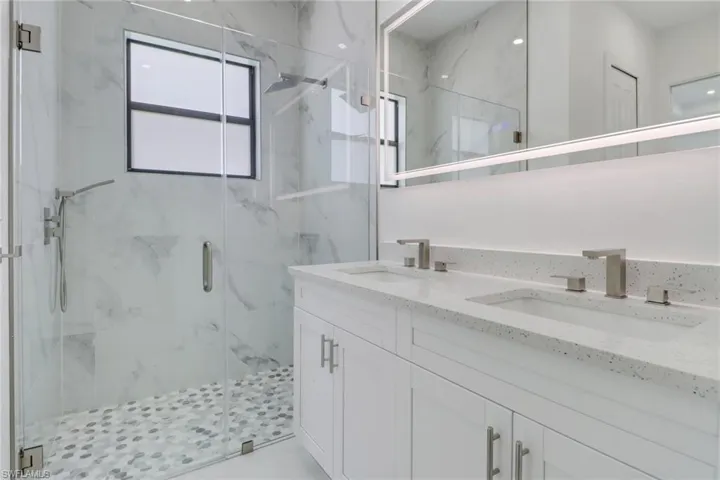 Full bath featuring double vanity, a sink, and a marble finish shower