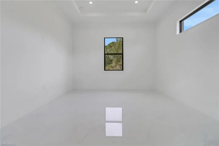 Empty room with a raised ceiling, marble finish floor, and recessed lighting