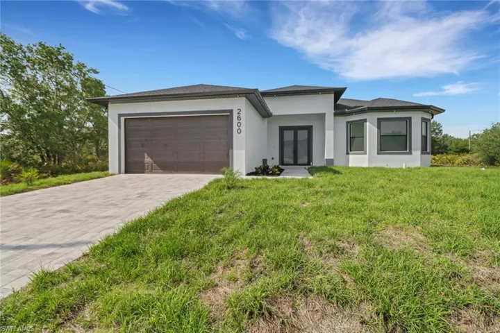 Prairie-style home featuring a garage, stucco siding, decorative driveway, and a front lawn