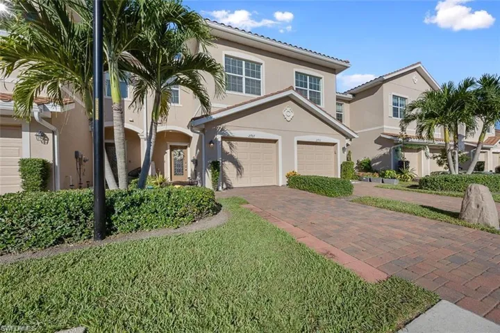 Stucco exterior with a tile roof, featuring a brick paver driveway and an integrated two-car garage