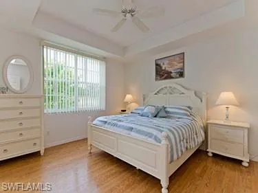 Bedroom with a raised ceiling, a ceiling fan, and light wood-style floors