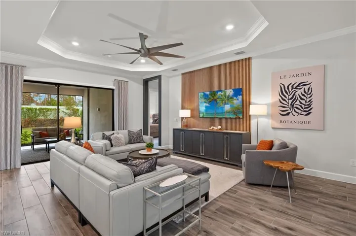 Living room with crown molding, a tray ceiling, ceiling fan, wood wall accent
