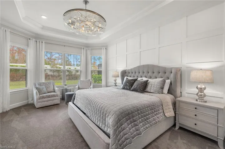Primary bedroom with bay window, tray ceiling, chandelier, crown molding and wood accent wall