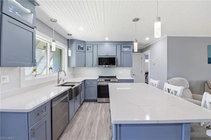 Kitchen featuring glass insert cabinets, a center island, a kitchen bar, light stone countertops, and stainless steel appliances.
