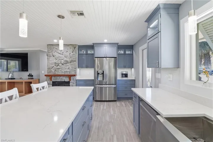 Kitchen with hanging light fixtures, stainless steel appliances, glass insert cabinets, light stone countertops, and wood ceiling.
