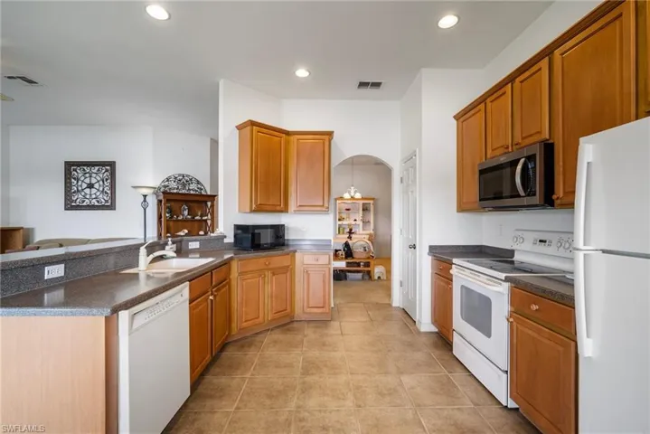 Kitchen with sink, white appliances, light tile patterned flooring, and hanging light fixtures