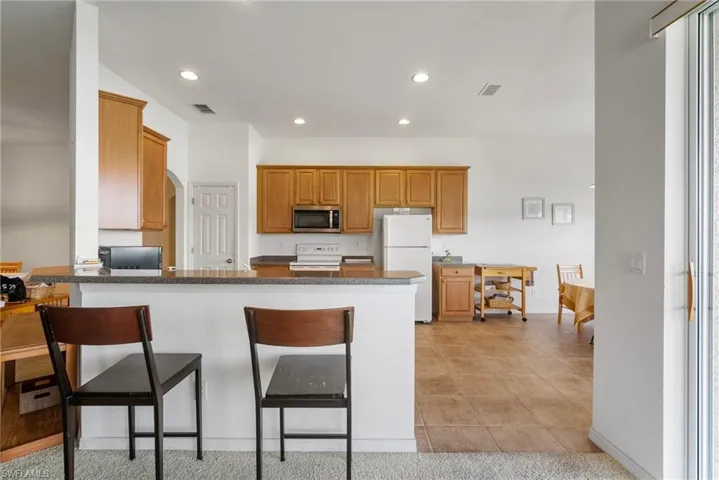 Kitchen with a kitchen breakfast bar, kitchen peninsula, white appliances, light tile patterned flooring, and dark stone countertops
