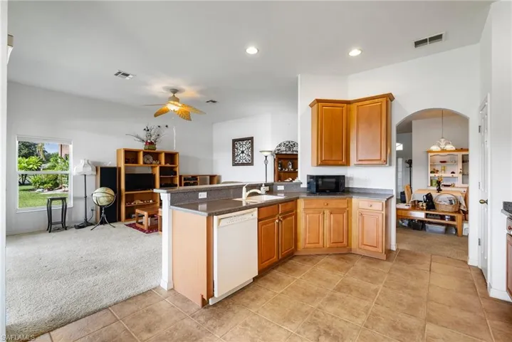 Kitchen featuring kitchen peninsula, ceiling fan, white dishwasher, and light carpet