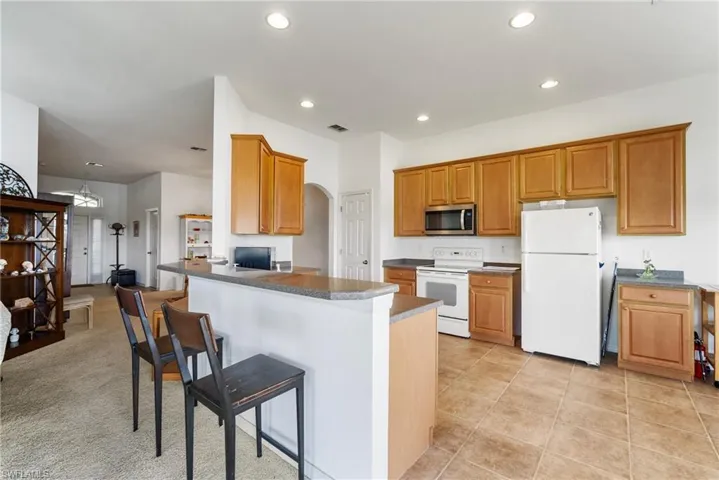 Kitchen featuring a kitchen bar, kitchen peninsula, light carpet, and white appliances