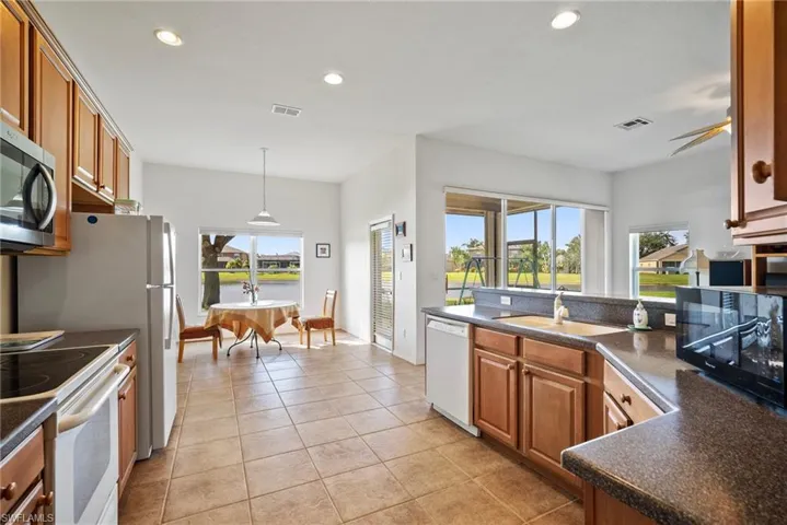 Kitchen with light tile patterned floors, sink, white appliances, and a healthy amount of sunlight