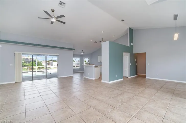 Unfurnished living room with a ceiling fan, light tile patterned floors, high vaulted ceiling, and baseboards.