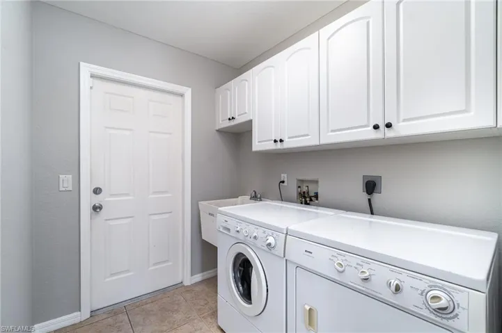 Laundry room with cabinet space, washer and dryer, baseboards, and light tile patterned flooring