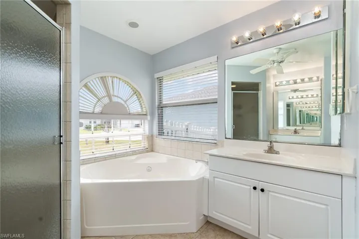 Primary Bathroom featuring a shower stall, ceiling fan, a garden tub, vanity, and lofted ceiling