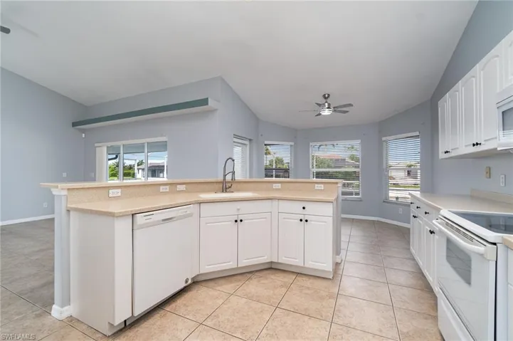 Kitchen with white appliances, a sink, light tile patterned floors, light countertops, and lofted ceiling