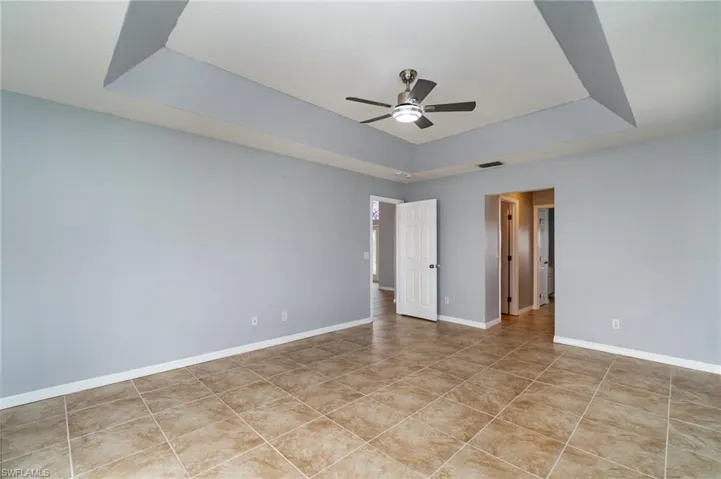 Primary Bedroom featuring a tray ceiling, a ceiling fan, light tile patterned floors, and baseboards