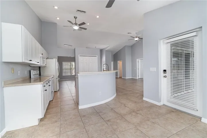 Looking into Kitchen from Breakfast Nook. Ceiling fan, light tile patterned flooring, light Corian countertops, and high vaulted ceiling