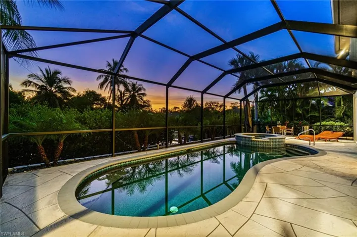 Pool at dusk with a pool with connected hot tub, a sunroom, a lanai, and a patio