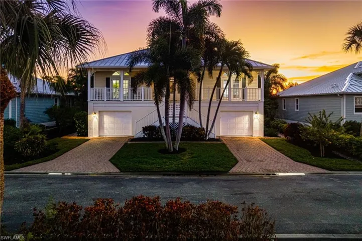 Coastal home featuring Key West style front staircase to main living level, a full front open porch for sunset viewing, decorative driveway, and dual attached deep tandem 4-car garages with extensive storage and additional living and lifestyle buildout potential.