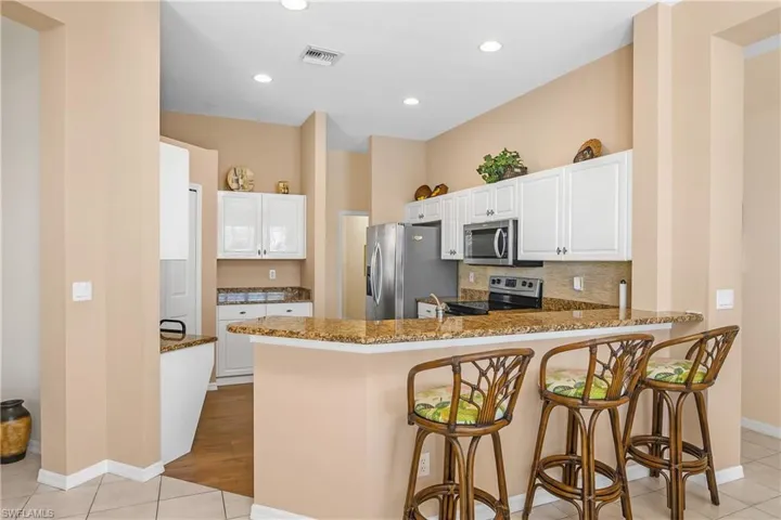 Kitchen featuring kitchen peninsula, appliances with stainless steel finishes, a kitchen bar, dark stone countertops, and white cabinetry