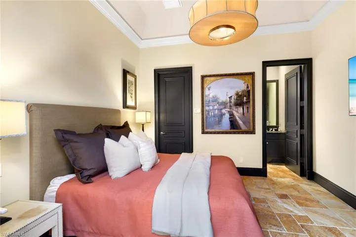 Bedroom with ornamental molding, stone tile flooring, and connected bathroom
