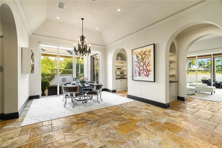Dining room featuring arched walkways, plenty of natural light, built in features, stone tile flooring, and crown molding