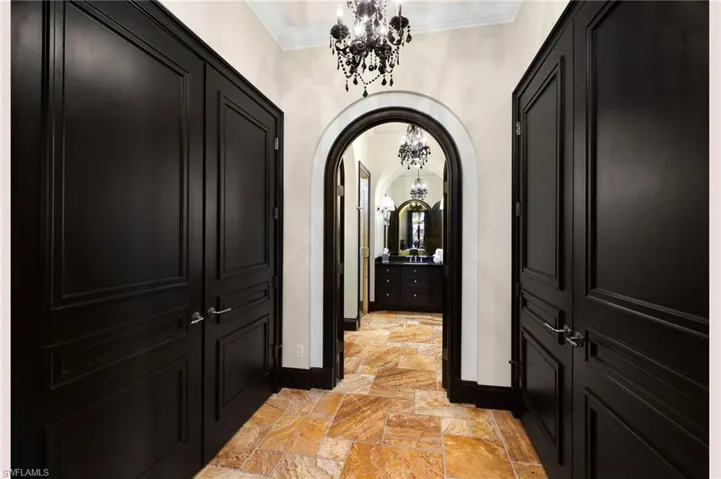 Hallway with a chandelier, arched walkways, ornamental molding, and stone tile flooring