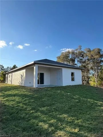 Back of property featuring stucco siding, a patio area, and a lawn