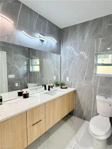 Bathroom with vanity, tile walls, plenty of natural light, light marble finish floors, and stone wall