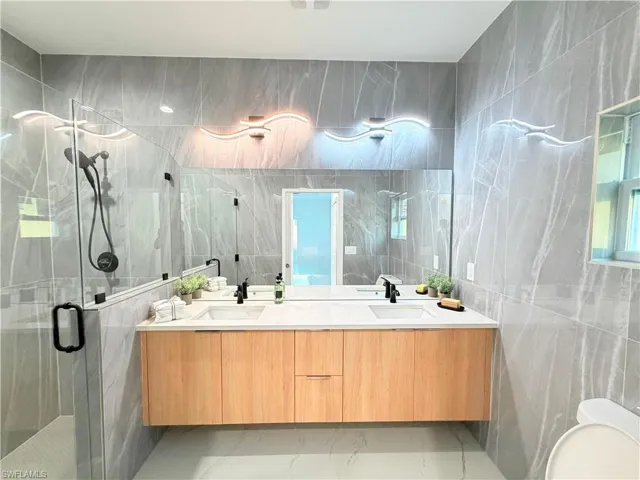Full bath featuring double vanity, tile walls, a stall shower, and light marble finish flooring