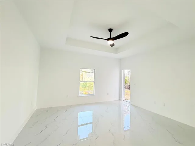 Spare room featuring light marble finish flooring, ceiling fan, and a raised ceiling