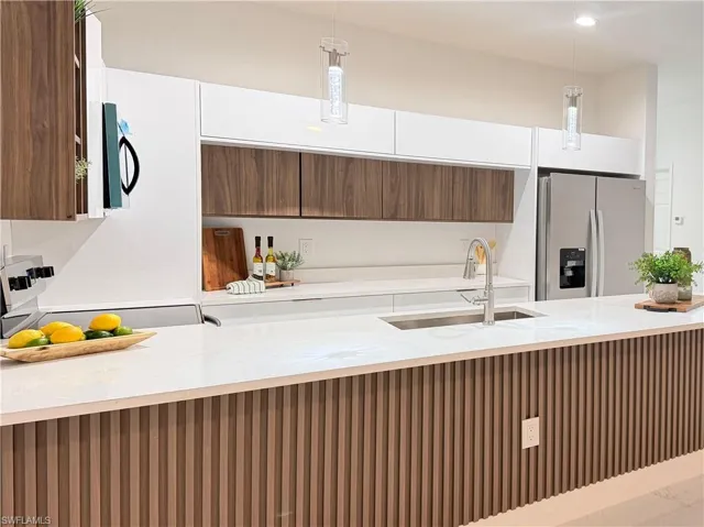 Kitchen with wood finish cabinetry, light stone countertops, stainless steel fridge, hanging light fixtures, and stove