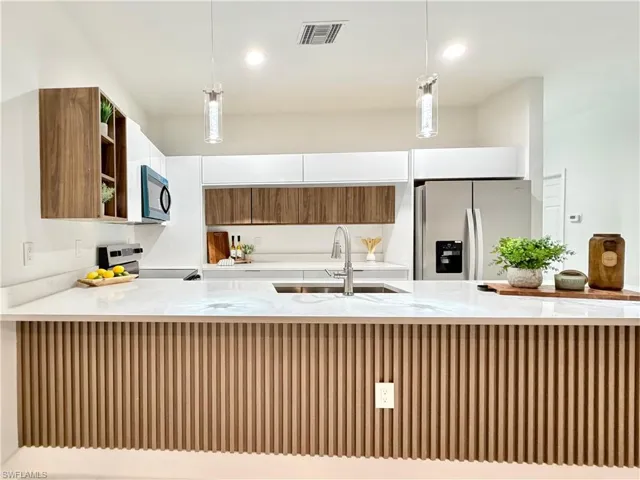 Kitchen featuring wood finish cabinetry, light stone counters, decorative light fixtures, and stainless steel appliances