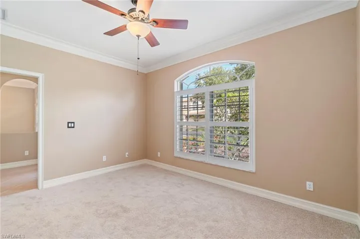 Empty room featuring light colored carpet, ornamental molding, a ceiling fan, and arched walkways