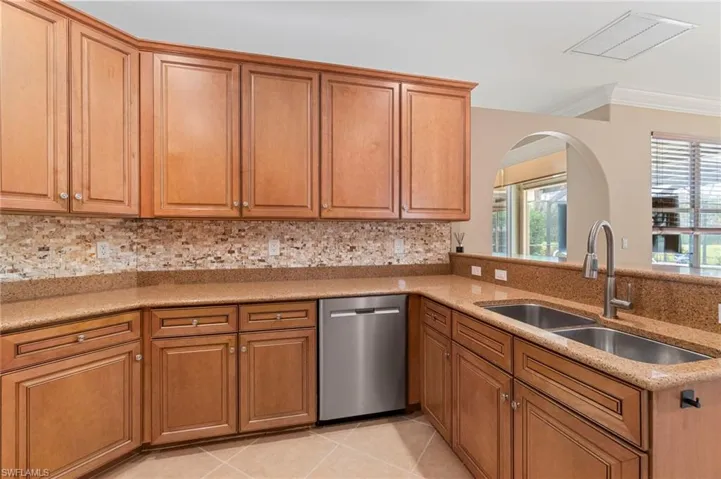 Kitchen with ornamental molding, stainless steel dishwasher, light tile patterned floors, tasteful backsplash, and brown cabinetry