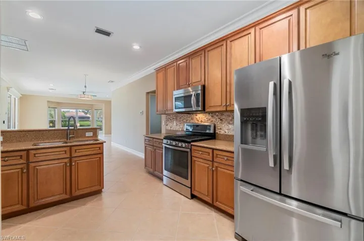 Kitchen featuring stainless steel appliances, brown cabinets, ornamental molding, light stone countertops, and light tile patterned floors
