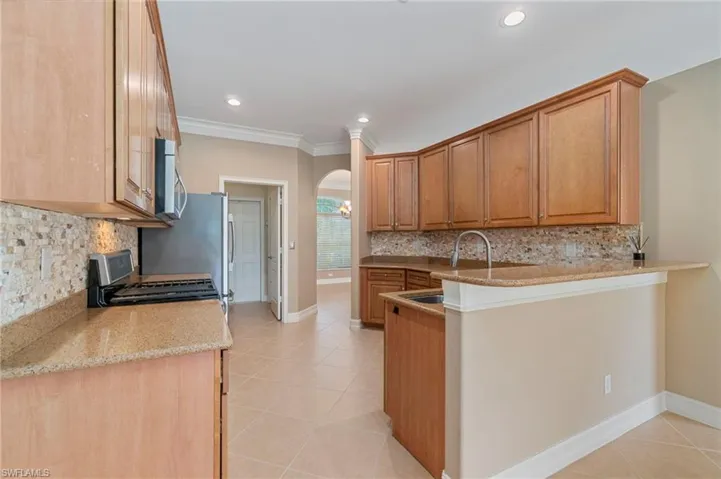Kitchen featuring decorative backsplash, arched walkways, light tile patterned floors, light stone counters, and recessed lighting