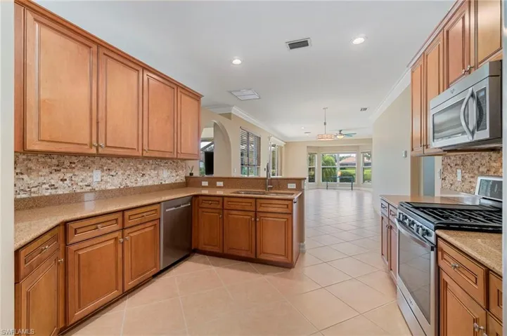 Kitchen with backsplash, appliances with stainless steel finishes, brown cabinets, ceiling fan, and a peninsula