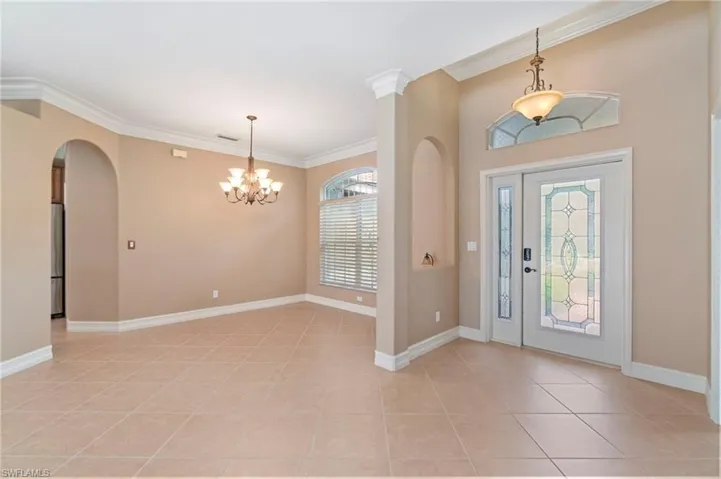 Entrance foyer featuring crown molding, arched walkways, light tile patterned flooring, and a chandelier