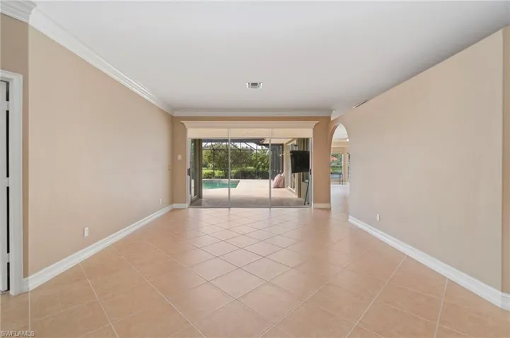 Unfurnished room featuring arched walkways, light tile patterned floors, and crown molding