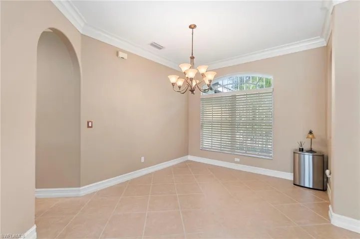 Empty room featuring a chandelier, ornamental molding, arched walkways, and light tile patterned flooring