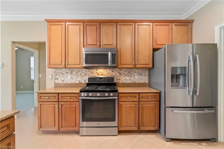 Kitchen featuring stainless steel appliances, crown molding, light tile patterned floors, and decorative backsplash