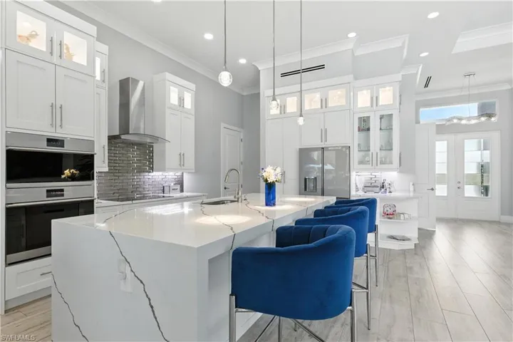 Kitchen with wall chimney range hood, appliances with stainless steel finishes, ornamental molding, tasteful backsplash, and an island with sink