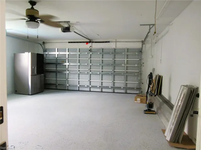 Garage with a garage door opener, ceiling fan, and stainless steel fridge with ice dispenser